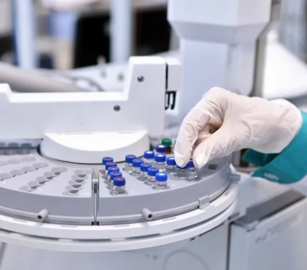 Quality control laboratory tech conducting chromatograph operation. A gloved hand makes an analysis on a gas chromatograph during the development of a new vaccine