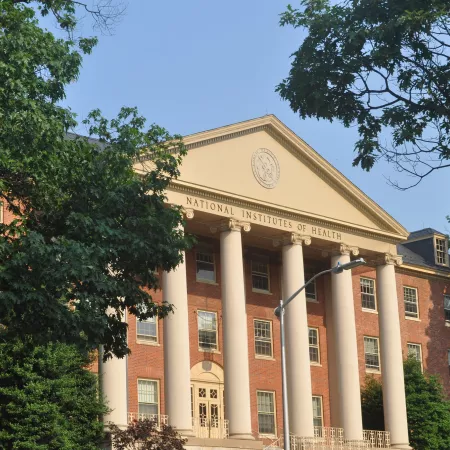 James H. Shannon Building (Building One), NIH campus, Bethesda, MD. A brick Georgian Revival building flanked by trees under a blue sky.