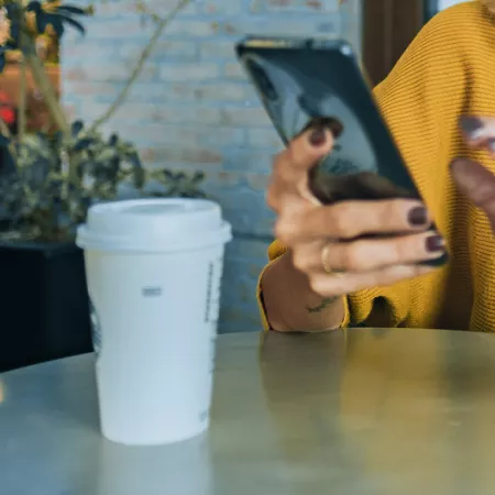 person looking at phone sitting at a cafe table with to-go coffee cup