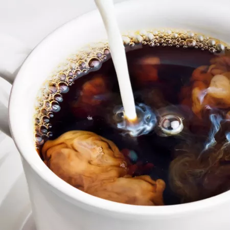 cup of coffee with creamer being pored in