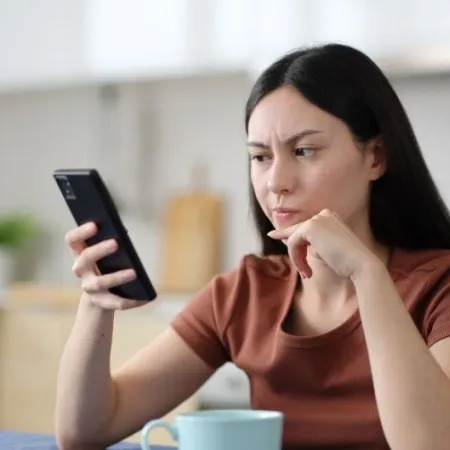 Woman looks skeptically at phone in kitchen