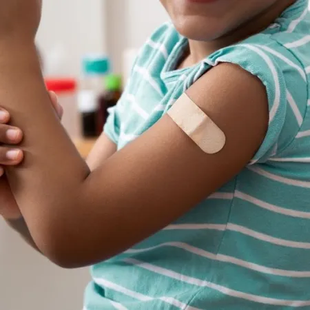 A Black child shows off their arm with a bandage over a vaccine injection site