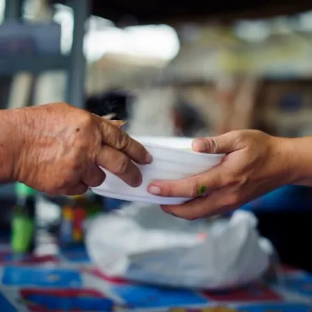 Closeup of a person handing a bowl of food to another person.