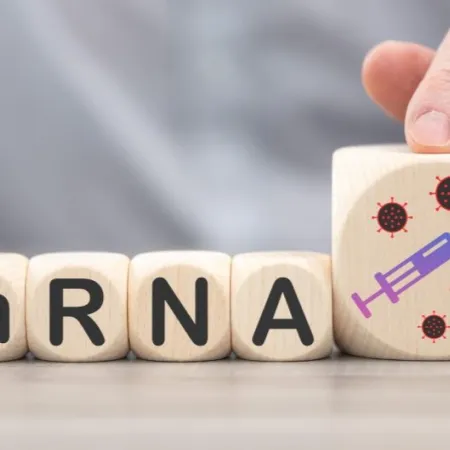 Wooden blocks spelling "mRNA" and a larger fifth block displaying a painted syringe on a table