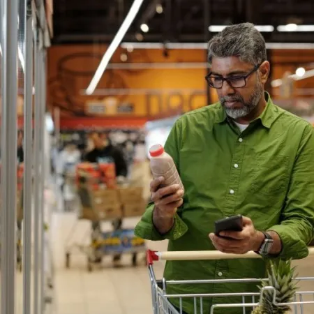 A man ina green shirt reads the label on a packaged food product in a grocery store