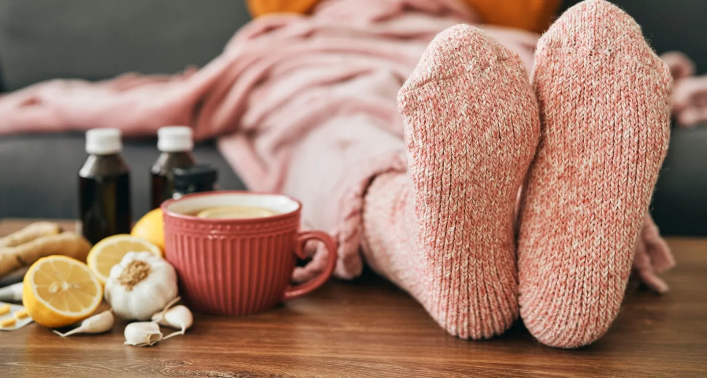 Feet wearing warm socks on a low table beside cold medicine and home remedies