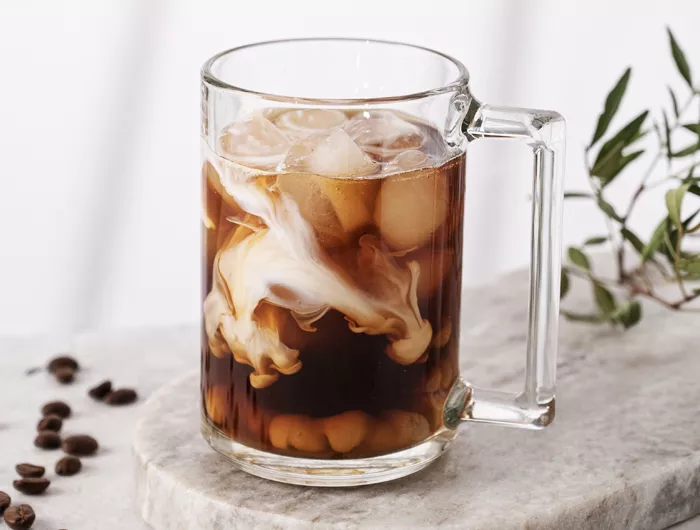 glass mug of iced coffee with cream on marble countertop